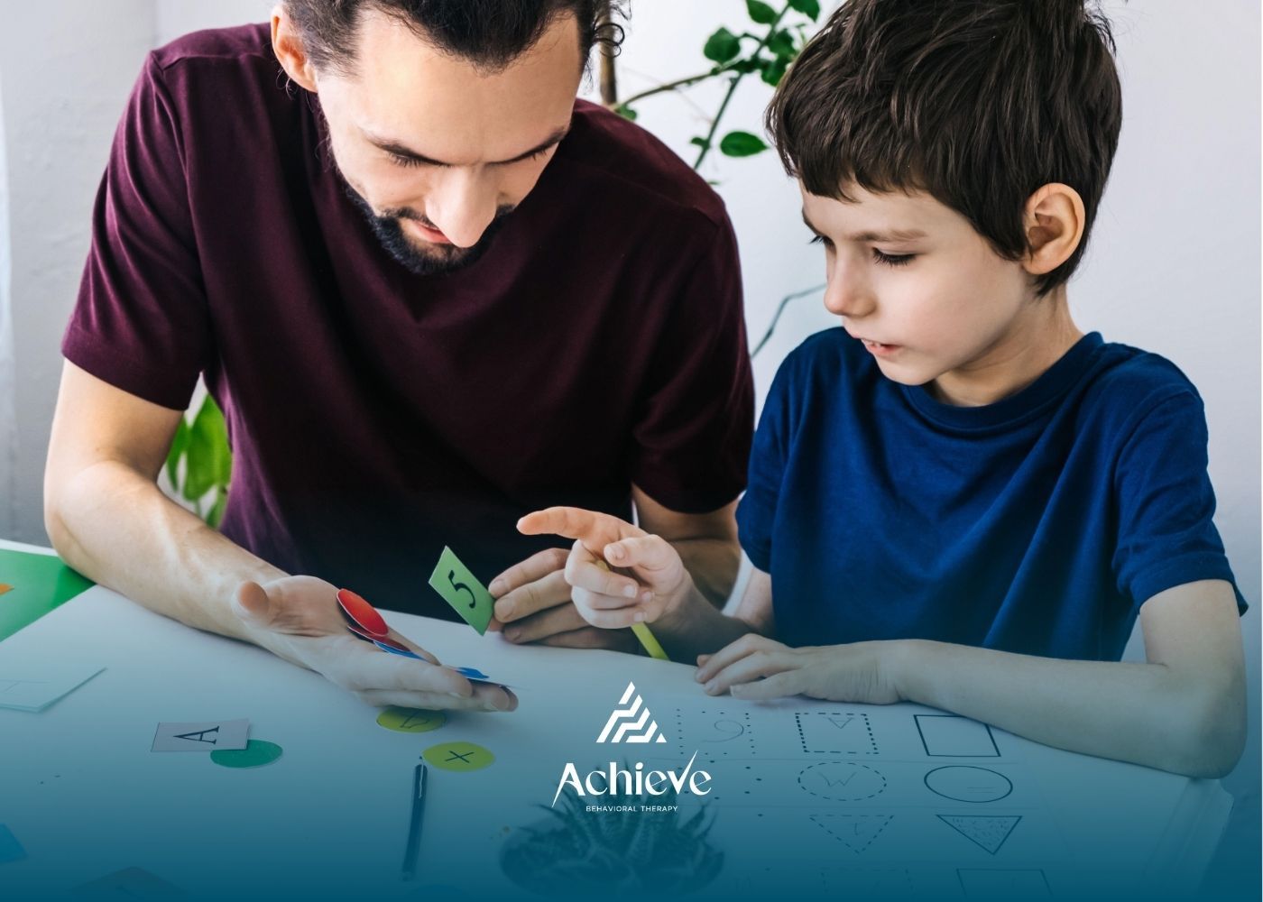 Man and boy at table, pointing at objects. Focus on learning, with Achieve logo.