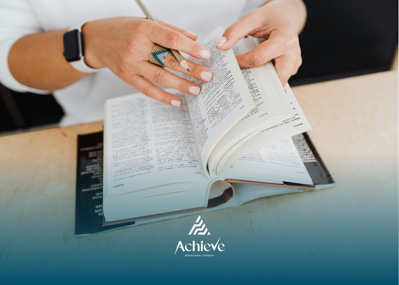 Hands flipping through pages of a book, next to a pen.