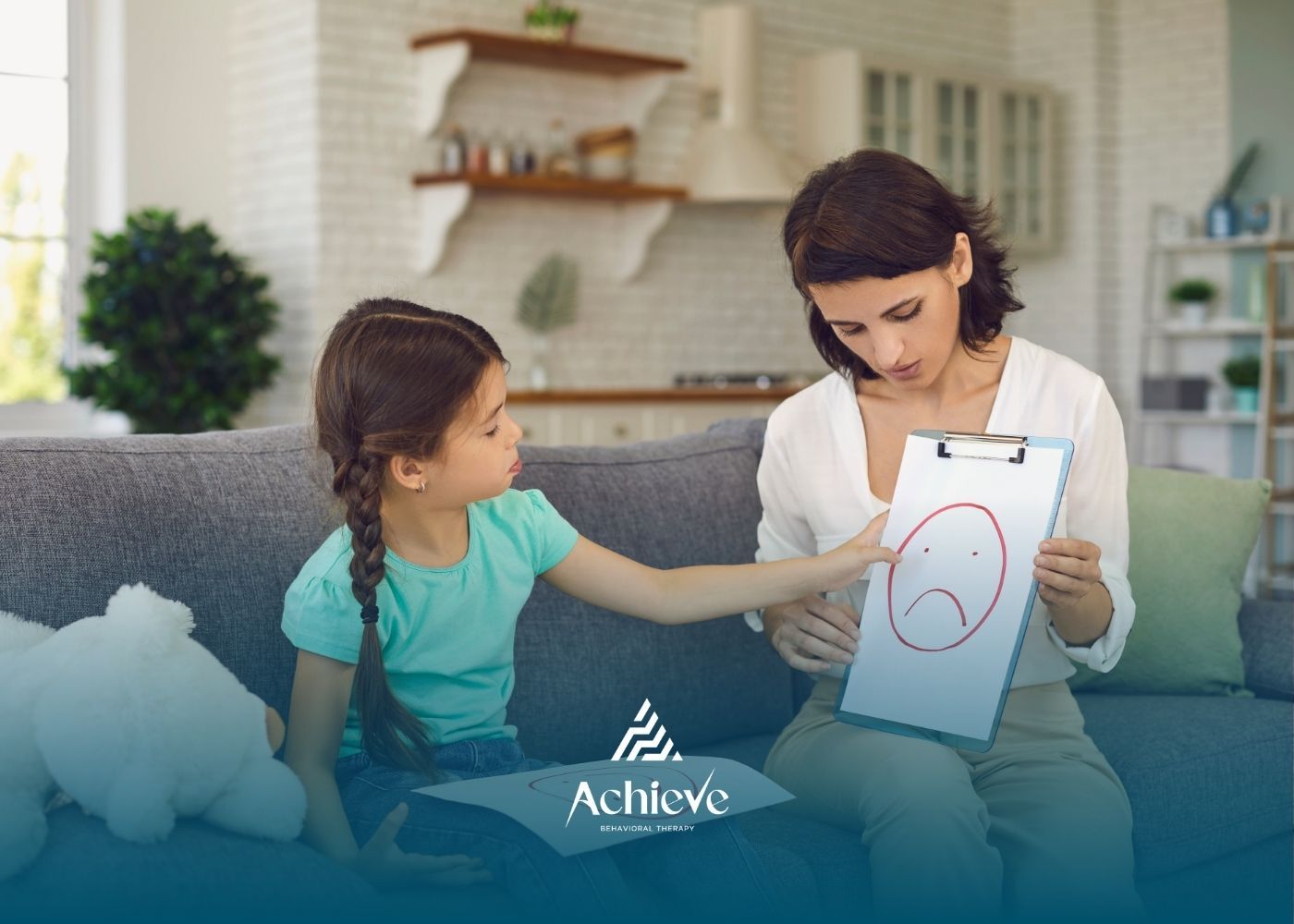 Woman shows sad face drawing to child on a couch, counseling session.