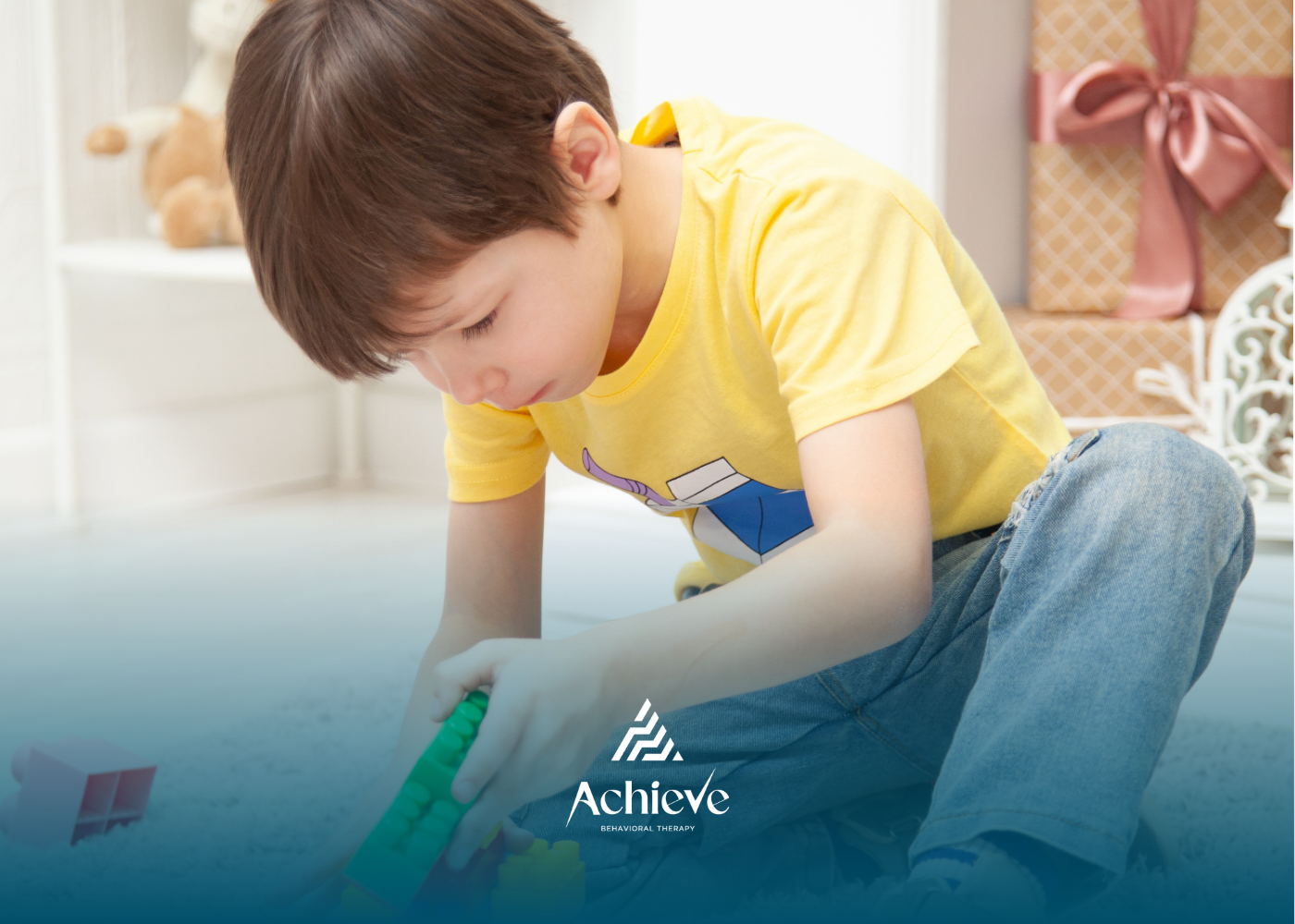 Boy in yellow shirt and jeans playing with toys on the floor, indoors.