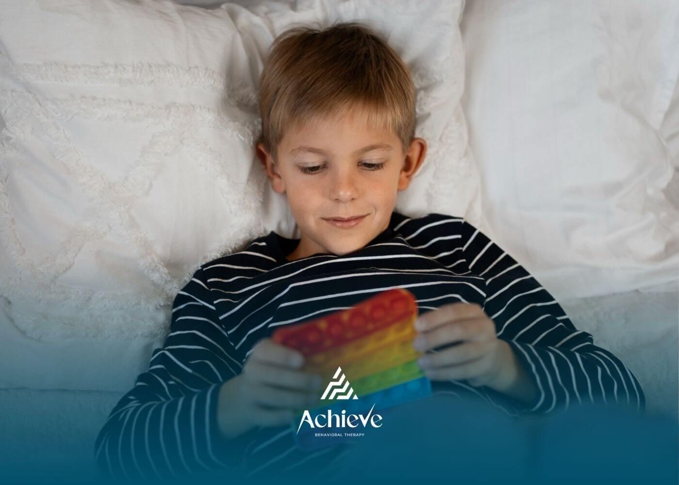 Boy with autism lying in bed playing with rainbow pop-it toy.