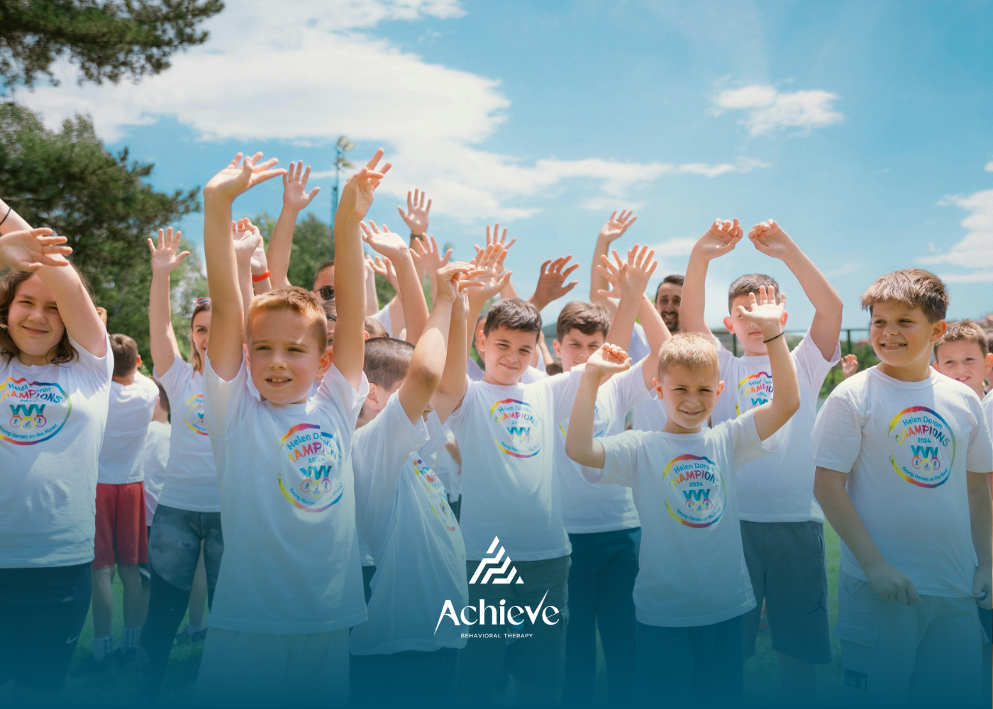 Children in white shirts with arms raised outdoors, blue sky. Divine Steps ABA logo at the bottom.