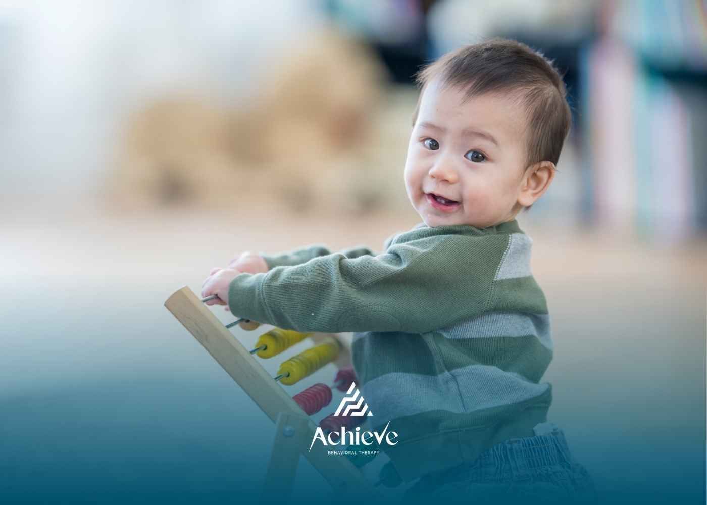 Baby playing with an abacus, smiling, wearing a green sweater. Soft-focus background.