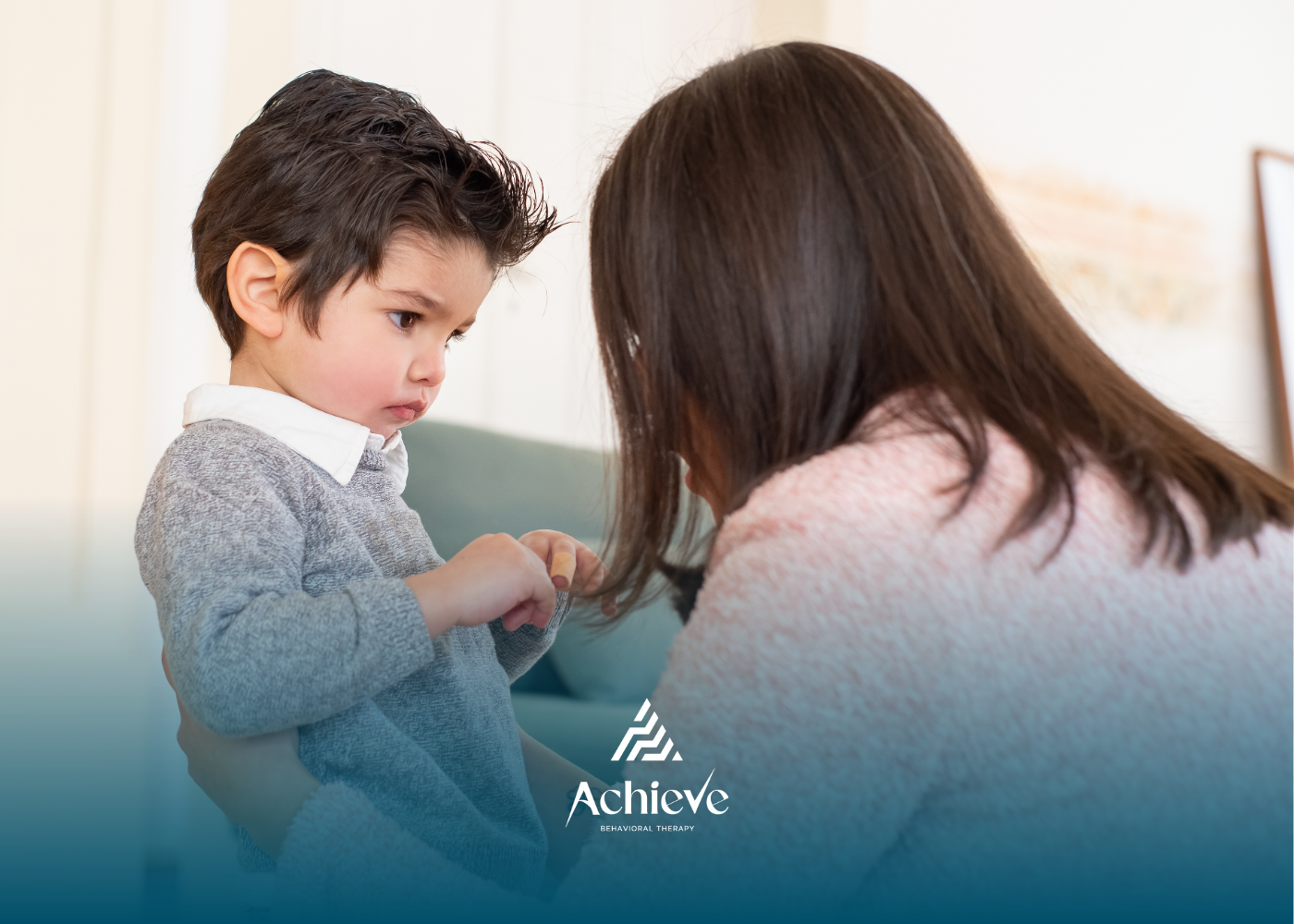A woman talks to a young child indoors. The child looks concerned.