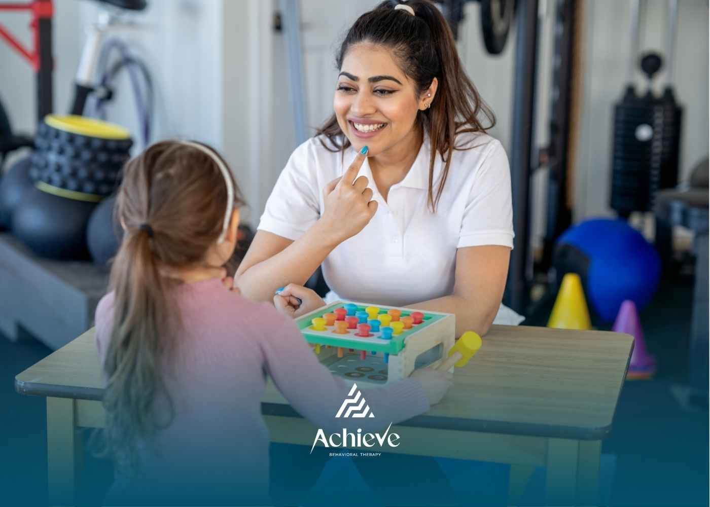 A smiling therapist in a white shirt interacts with a child using colorful educational toys on a tab