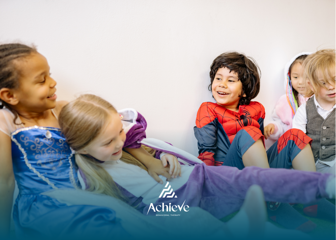 Children in costumes laugh and play together against a white wall.