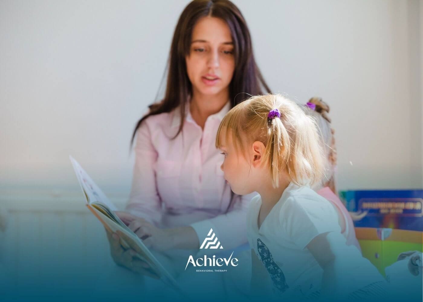 Therapist reading a book to a young child with autism sitting beside them.