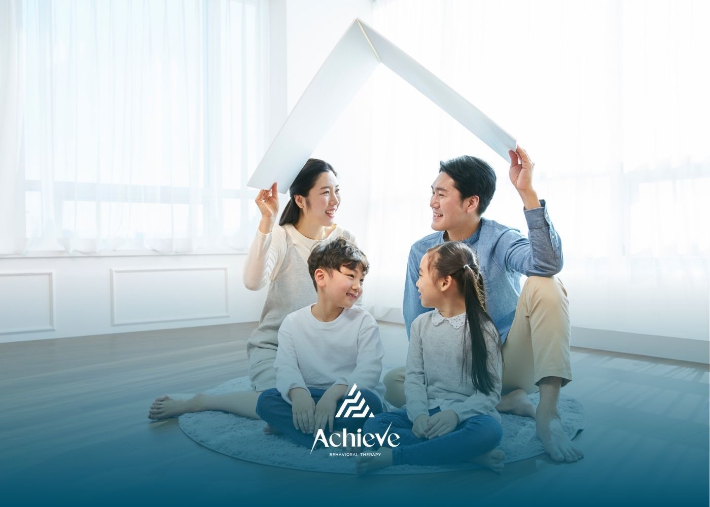 Family under a paper house: parents and children smiling, indoors.