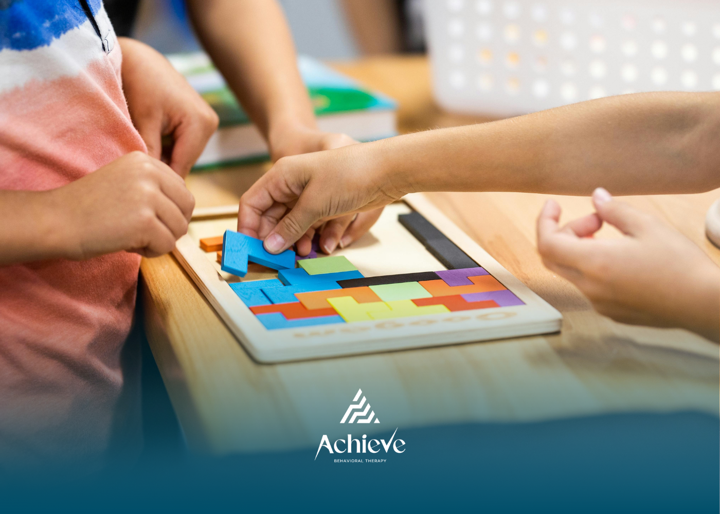 Hands assembling a colorful wooden puzzle on a table in a classroom-like setting.