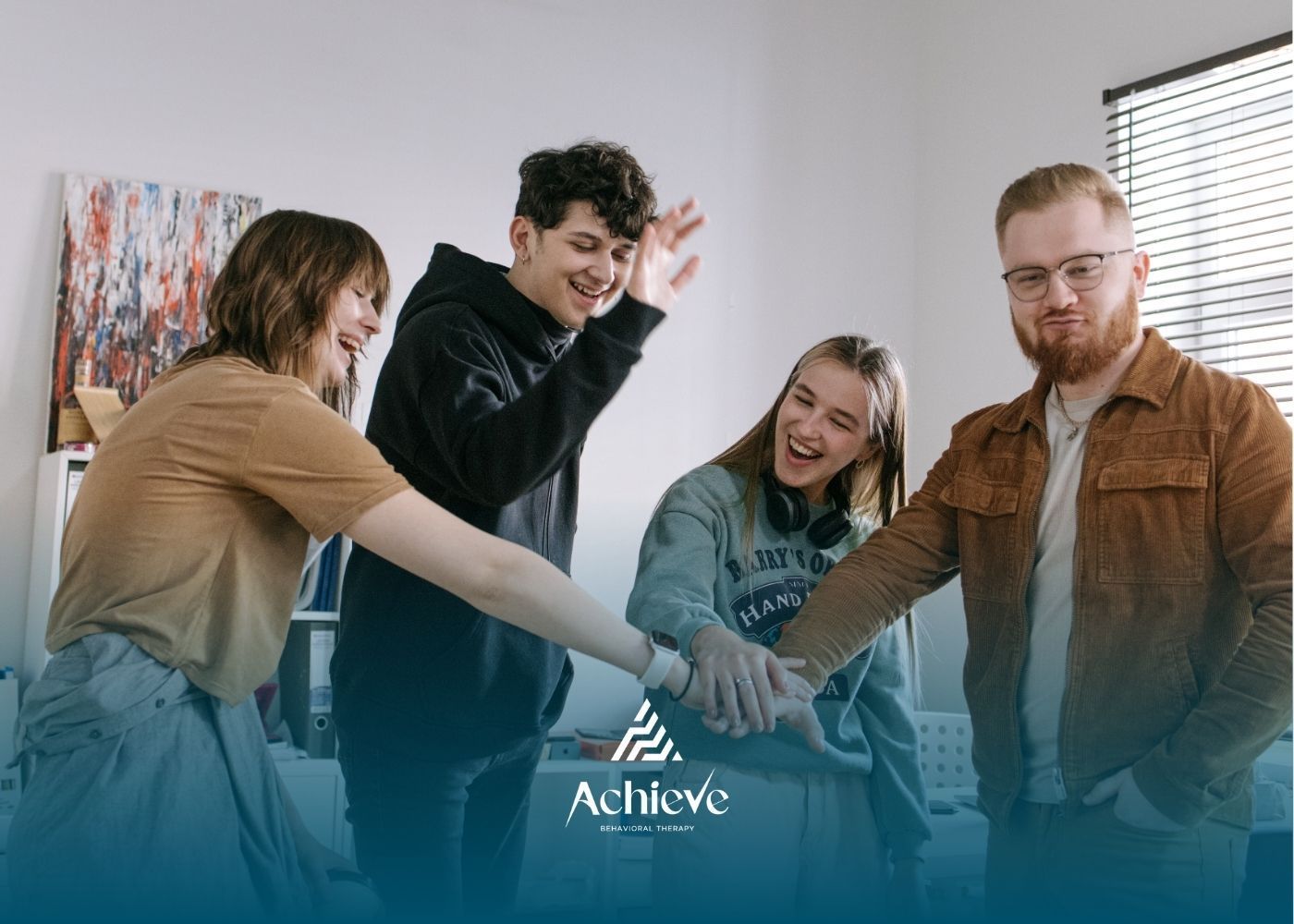 Four people with hands together, smiling, in a bright room.