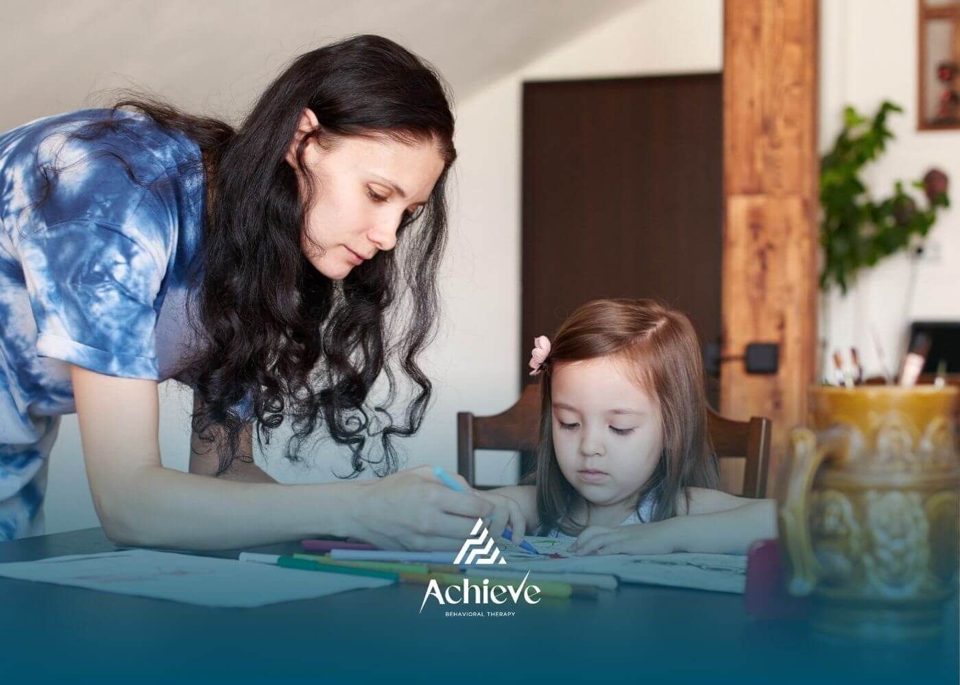 Female BCBA helping autistic girl with coloring at table in ABA therapy.