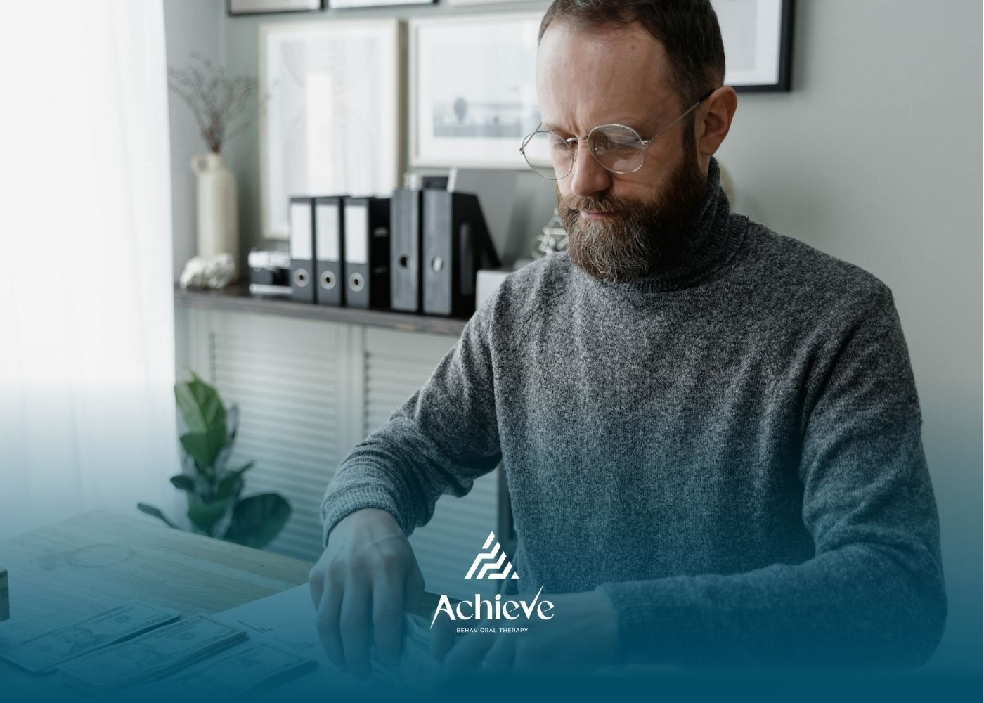 ABA therapist in gray sweater counts stacks of U.S. dollar bills at a desk in a modern office