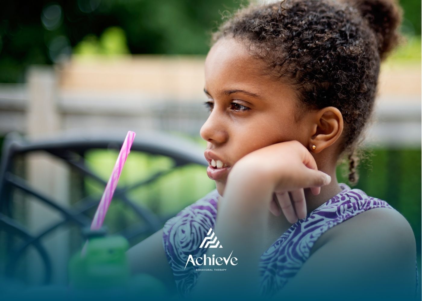 Girl with a drink looks thoughtful, resting her chin on her hand, outdoors.