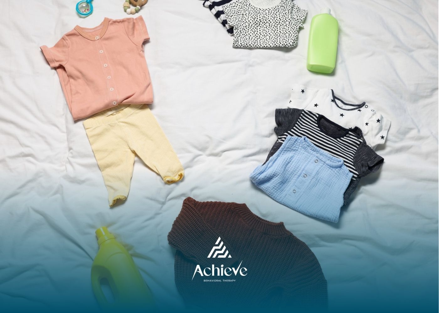 Baby clothes in various colors, a green bottle, and a toy on a white blanket.