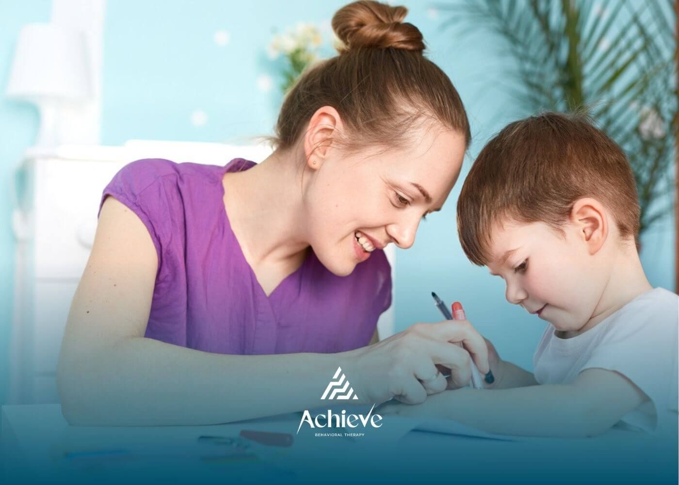 ABA therapist helping young boy write with pencil at desk in ABA therapy.
