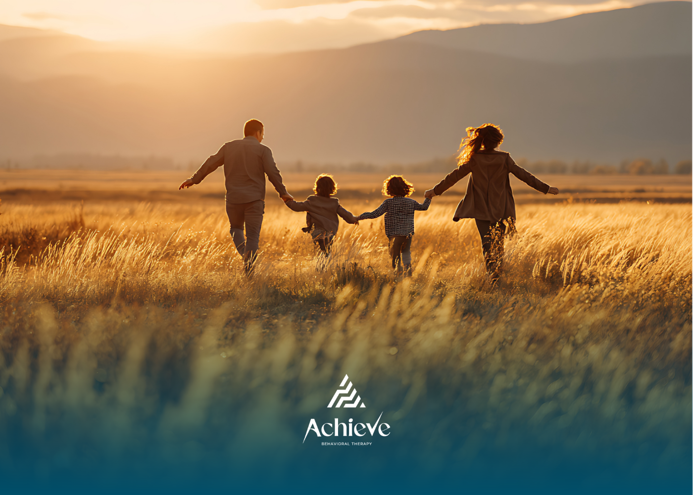 A family holds hands while running through a golden field at sunset.