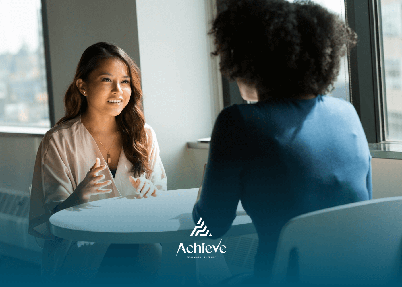 Two people seated at round table in bright room, engaged in a focused behavioral therapy session.