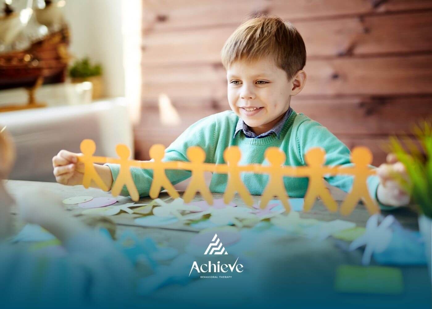 Autistic boy smiling while holding paper chain of people in ABA therapy.