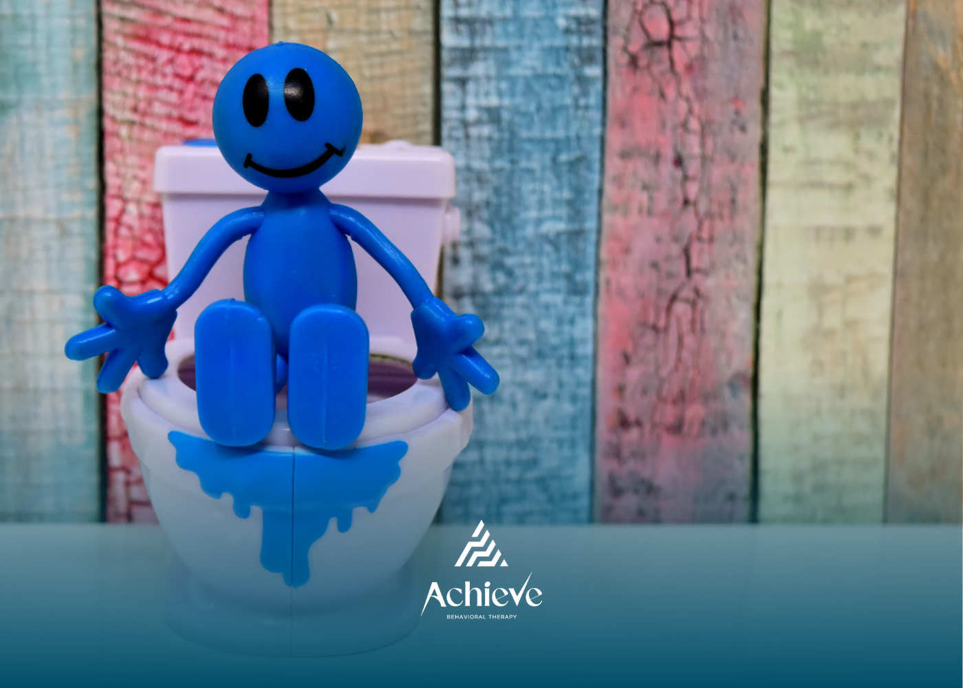 Blue smiling figurine sitting on a white toilet against a pastel wooden backdrop