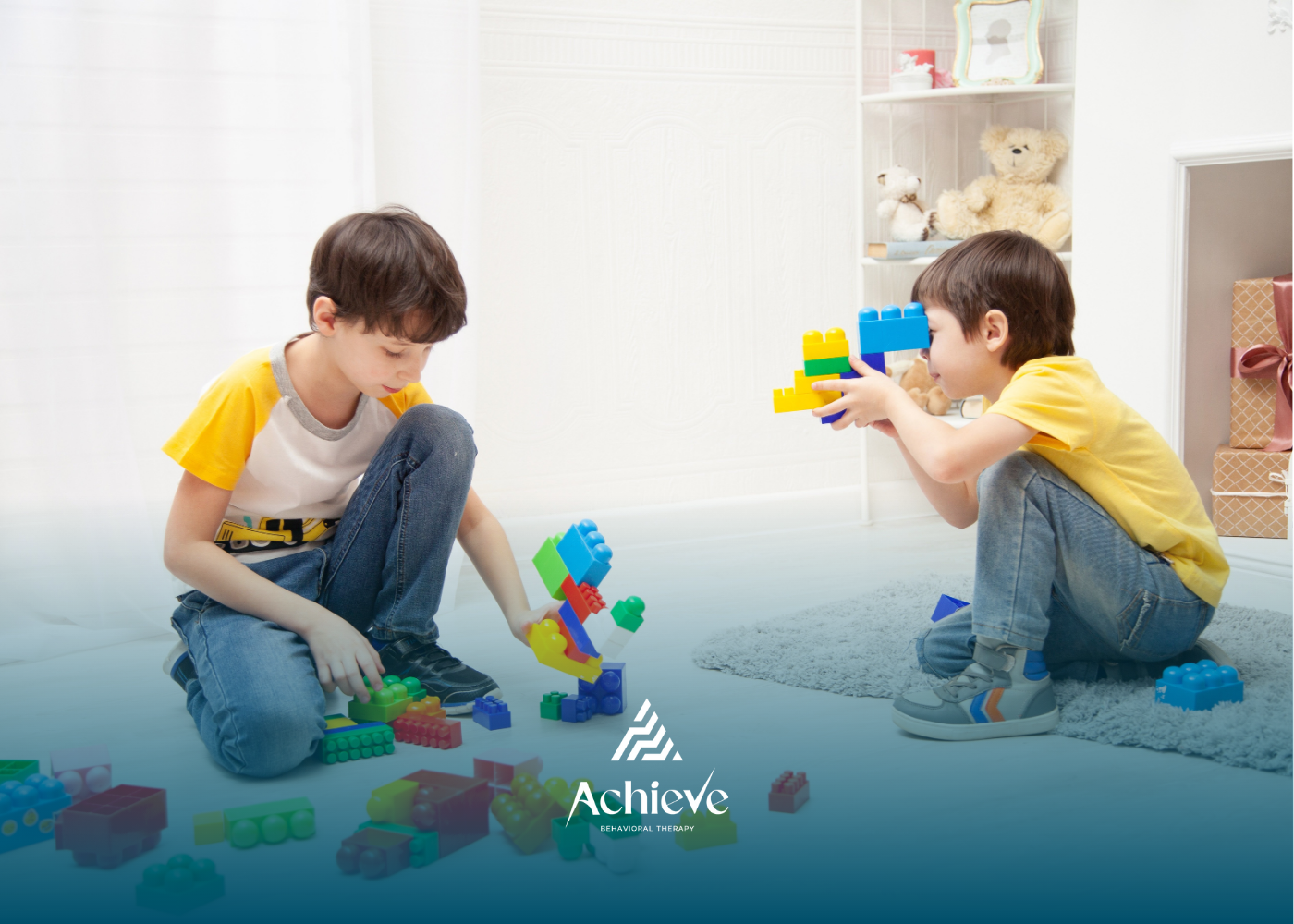 Two children playing with colorful building blocks on a rug, in a bright room. One is building, the other looks on.