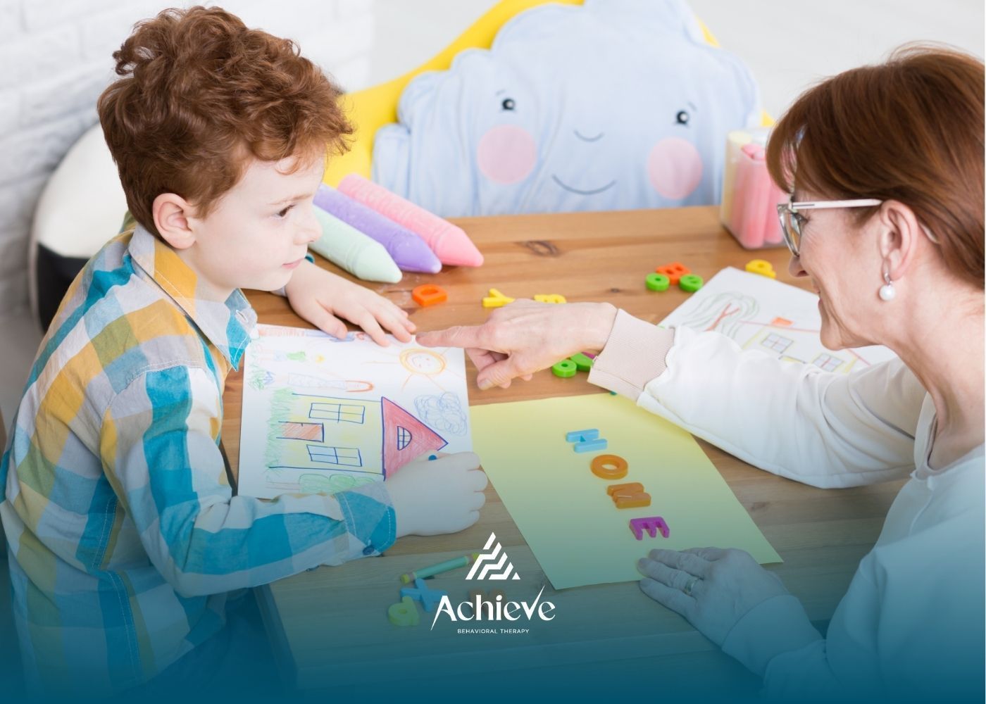 Boy at table with woman, pointing at letters; colored drawings and plush cloud in background.
