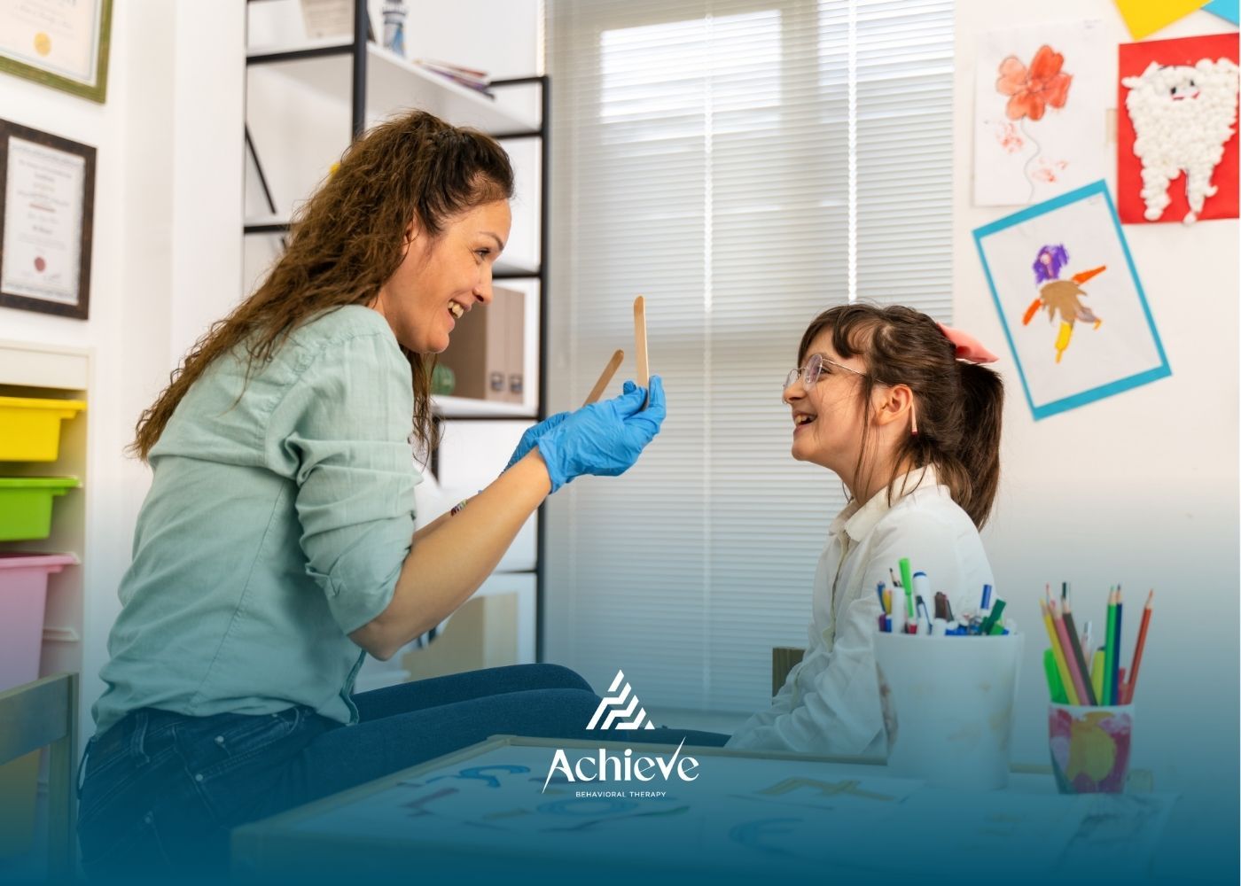 A clinician wearing blue gloves holds sticks for a child during a therapy session in an office with colorful wall art.