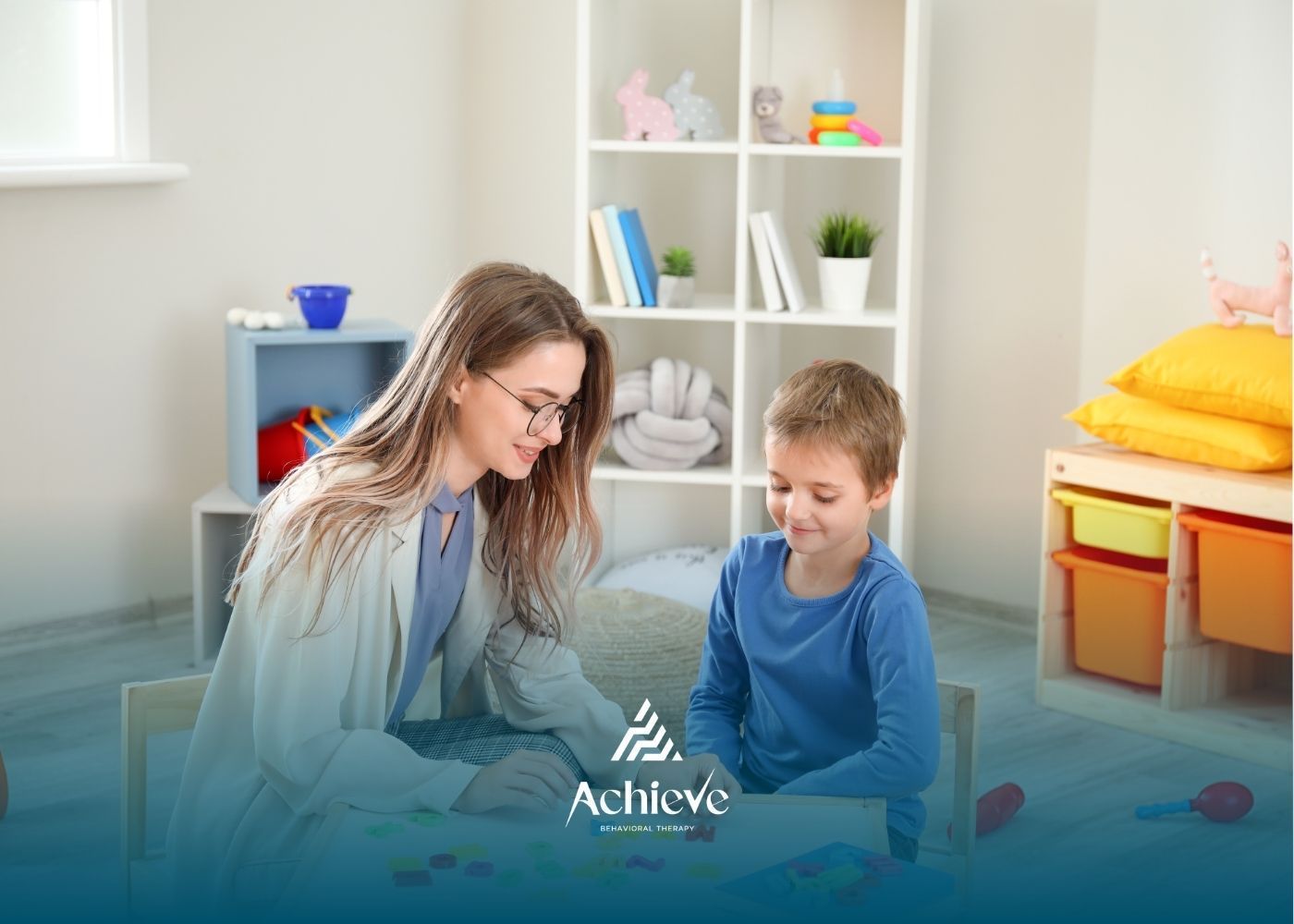 Woman with glasses and child at a table in a therapy setting. Bookshelf in the background.