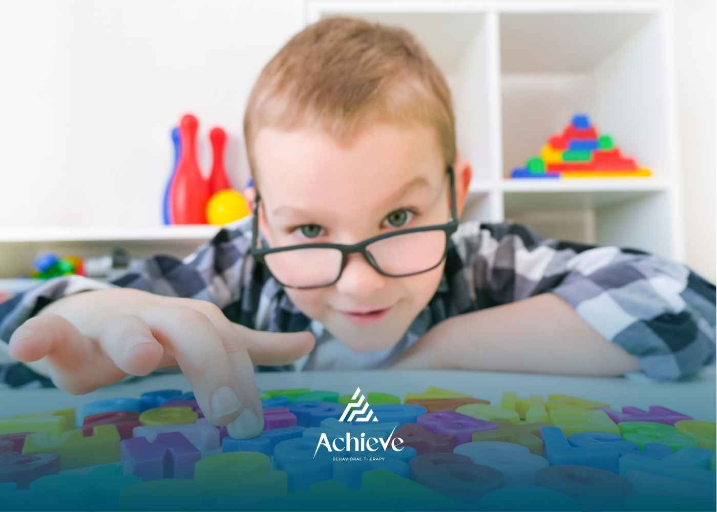 A child with glasses concentrates on colorful alphabet blocks on a table.