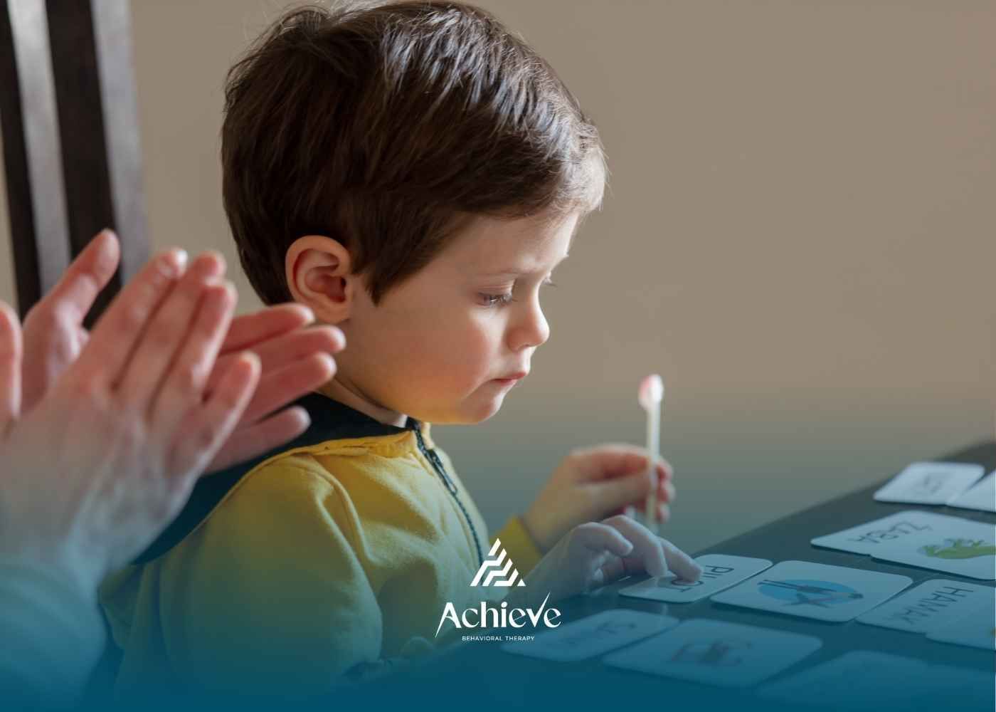 A young boy concentrates on cards with a light, while a hand claps in the background, indoors.