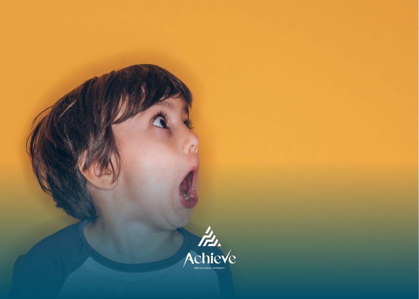 An autistic young boy with wide eyes and open mouth looks up against a bright orange background.
