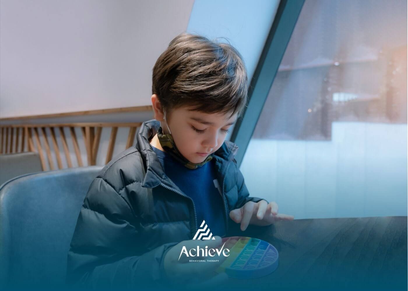 Autistic young boy focuses on playing with a colorful pop-it fidget toy in a cafe after ABA therapy.