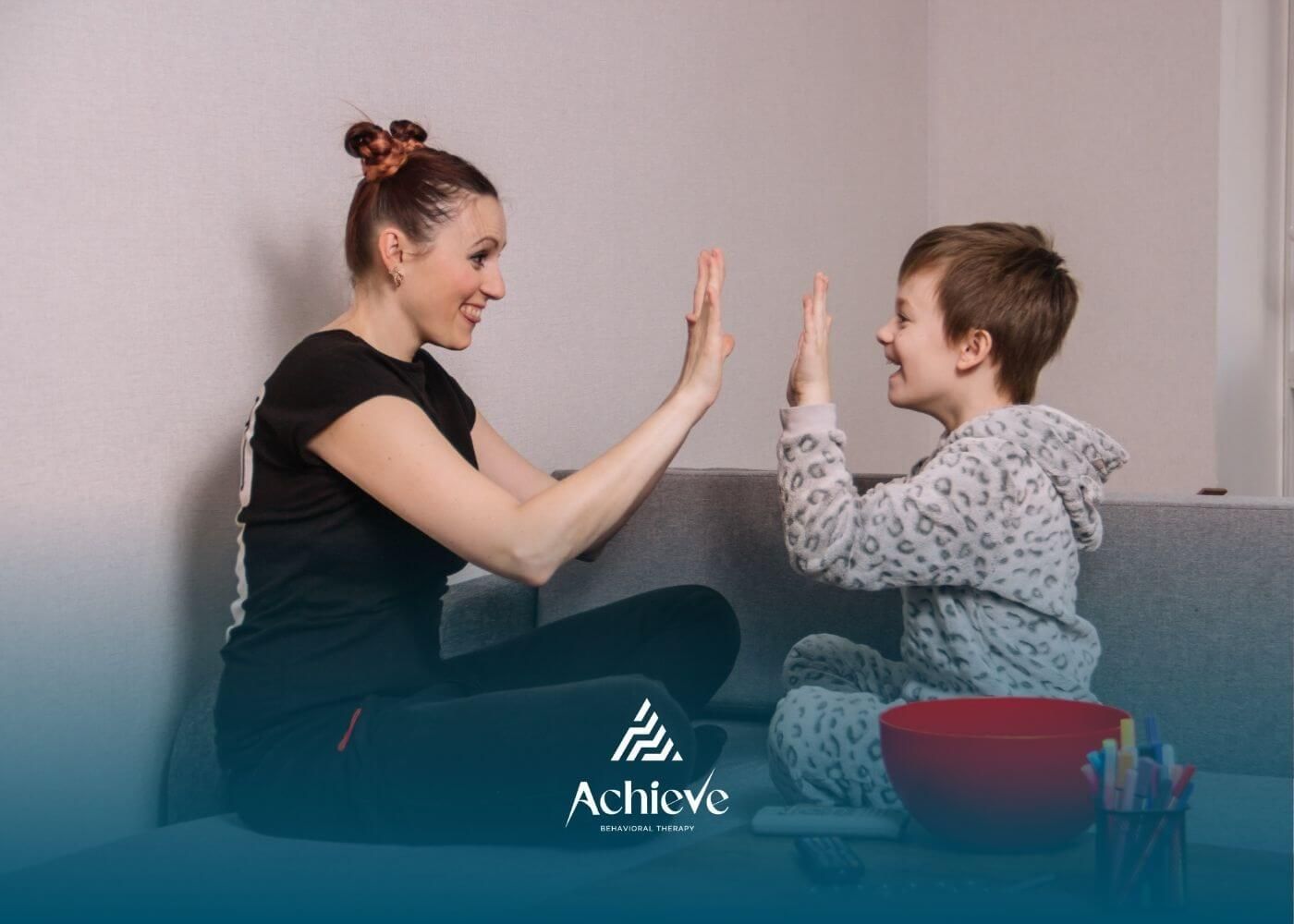 A BCBA and boy with autism smiling while playing a hand-clapping game in ABA therapy.