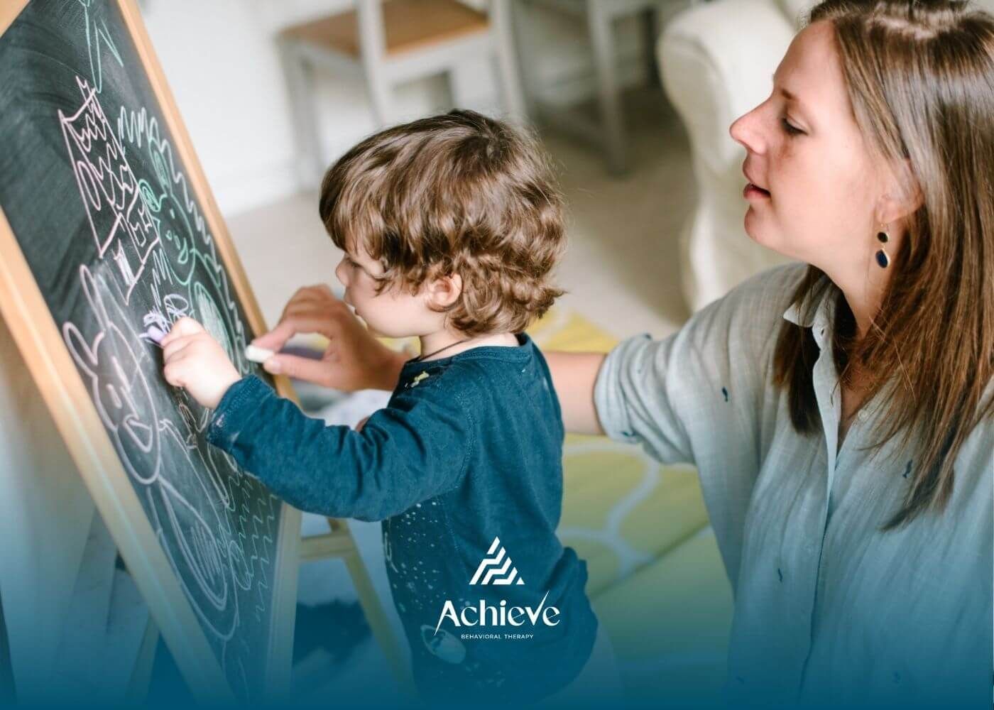 Caregiver helping a young child with autism draw on a chalkboard.