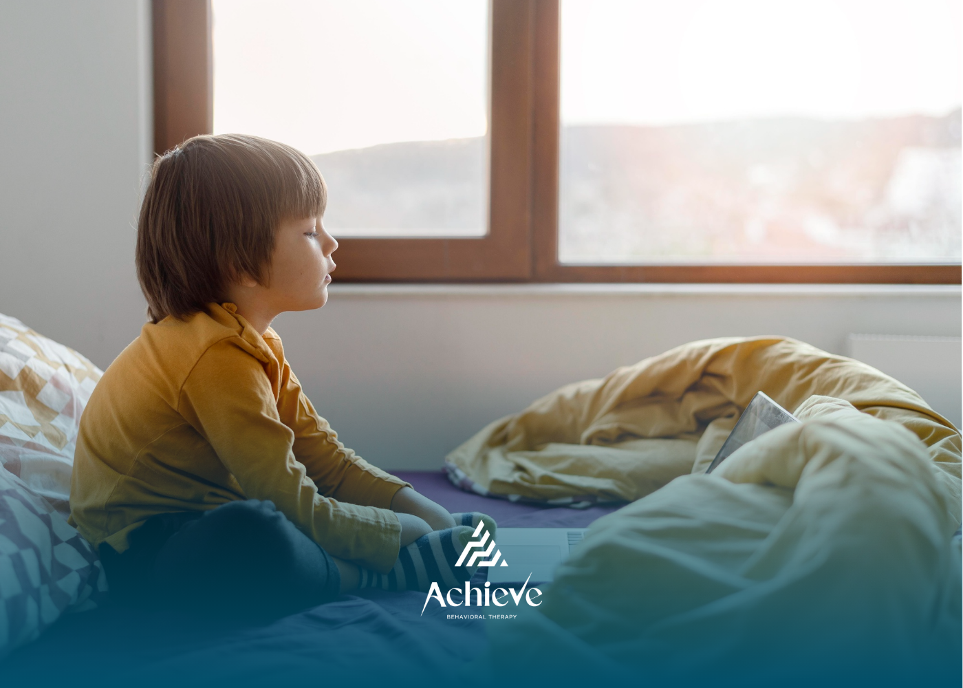 A child sitting on a bed, looking out a window.