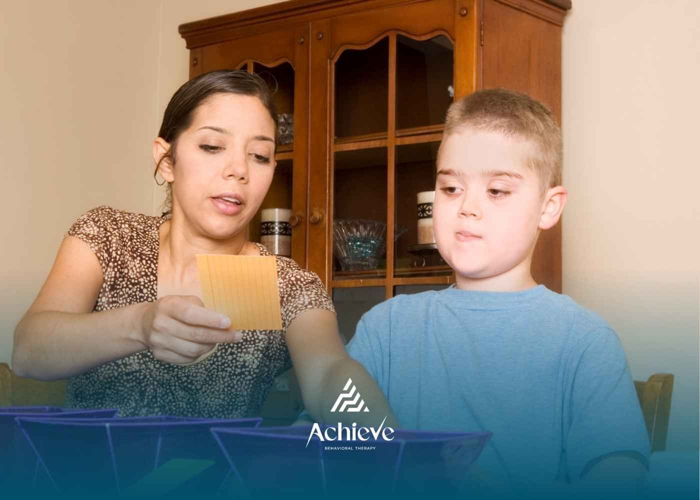 Woman teaching a young boy with Down syndrome at a table, sorting cards.