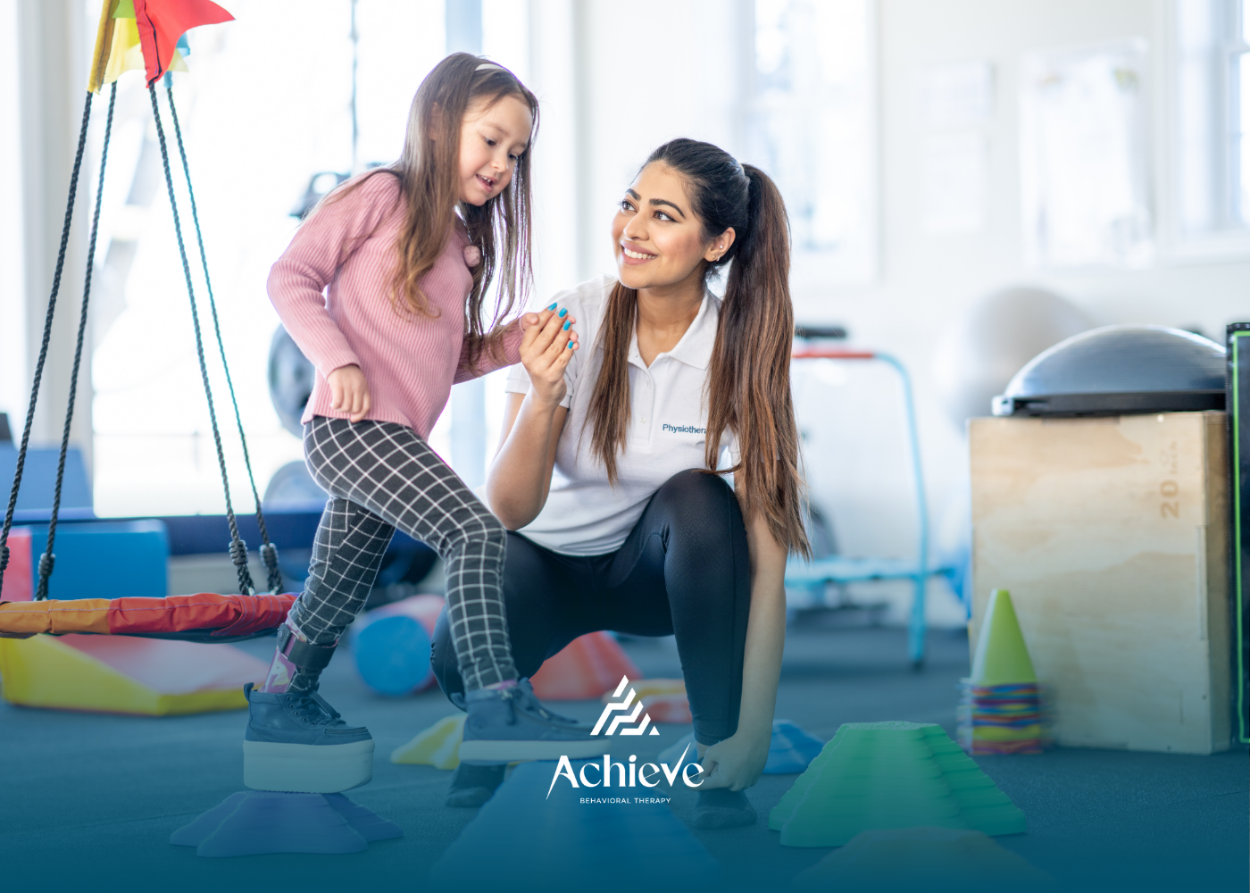 Therapist assists a girl with balance practice in a therapy room, smiling.