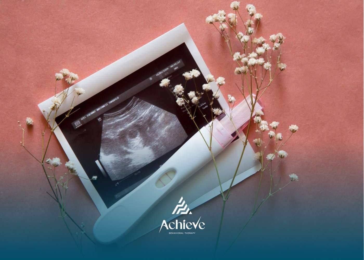 Pregnancy test, ultrasound image, and flowers on pink surface.