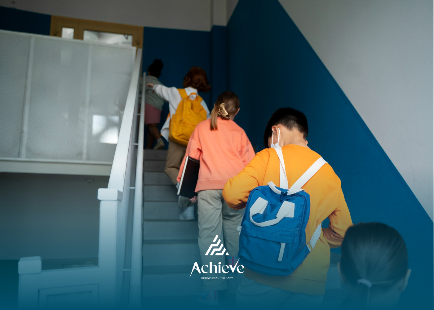 Students with backpacks walking up a staircase in a building with blue and white walls.