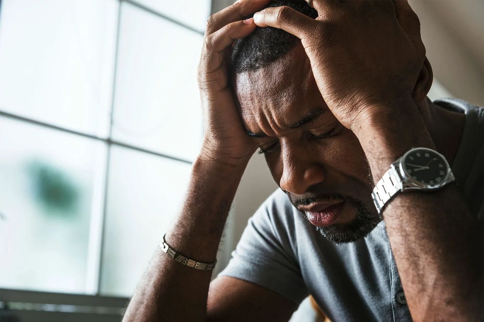 A man is holding his head in his hands while wearing a watch.