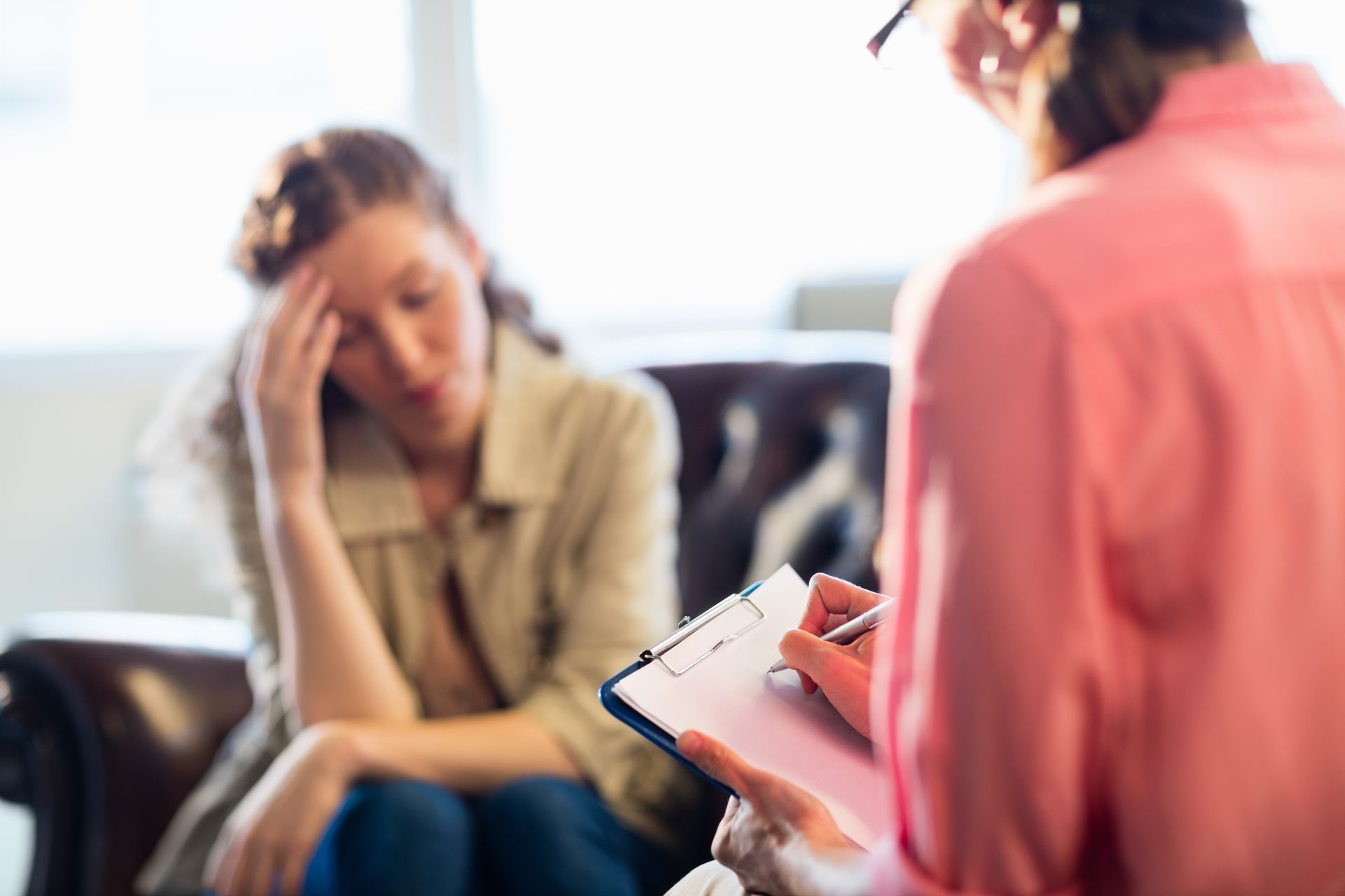 A woman is sitting on a couch talking to a female psychologist.