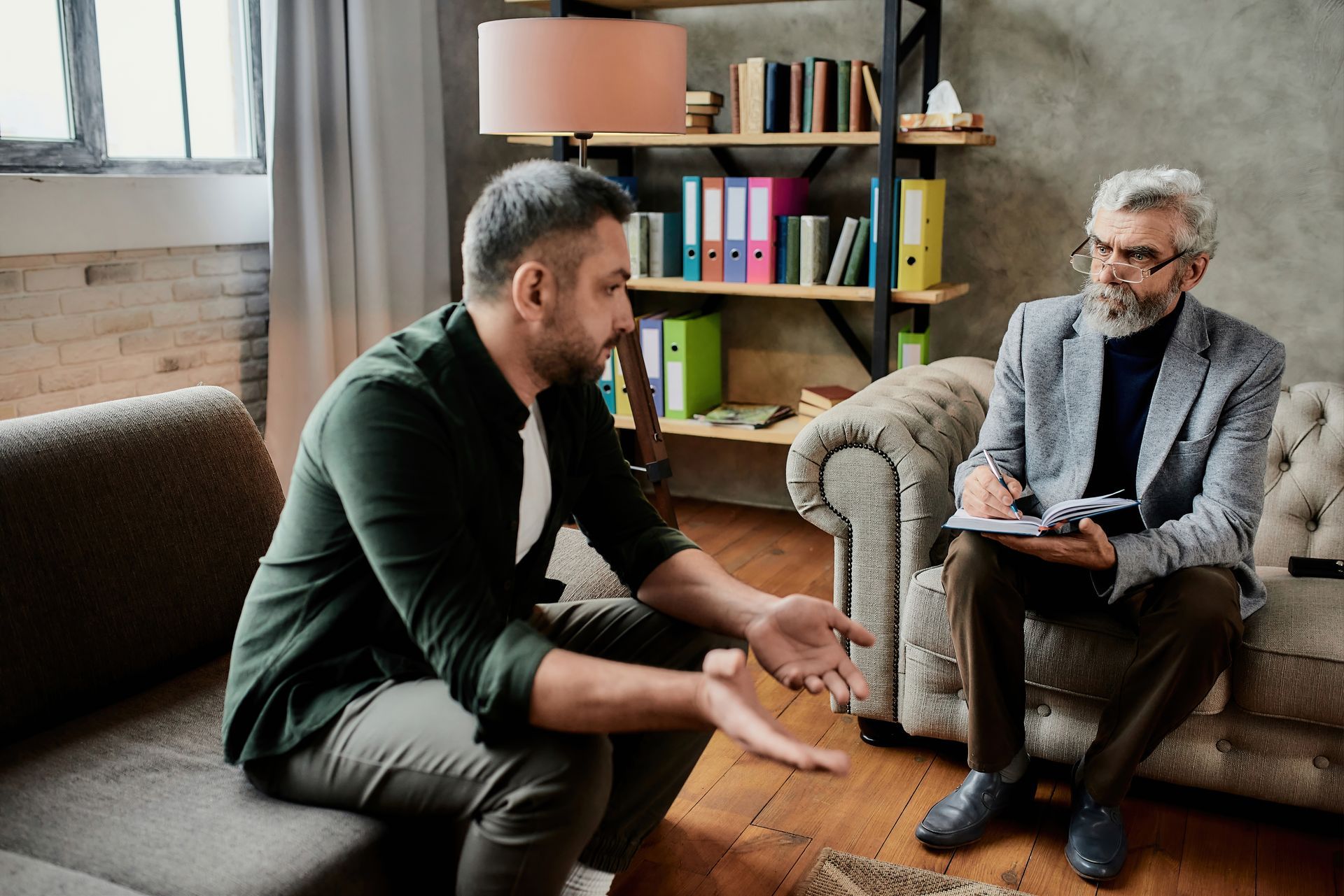 A man is sitting on a couch talking to a man in a suit.