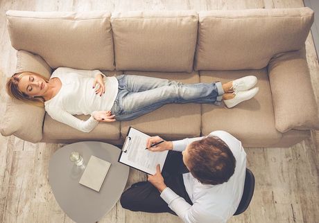 A woman is laying on a couch talking to a man.