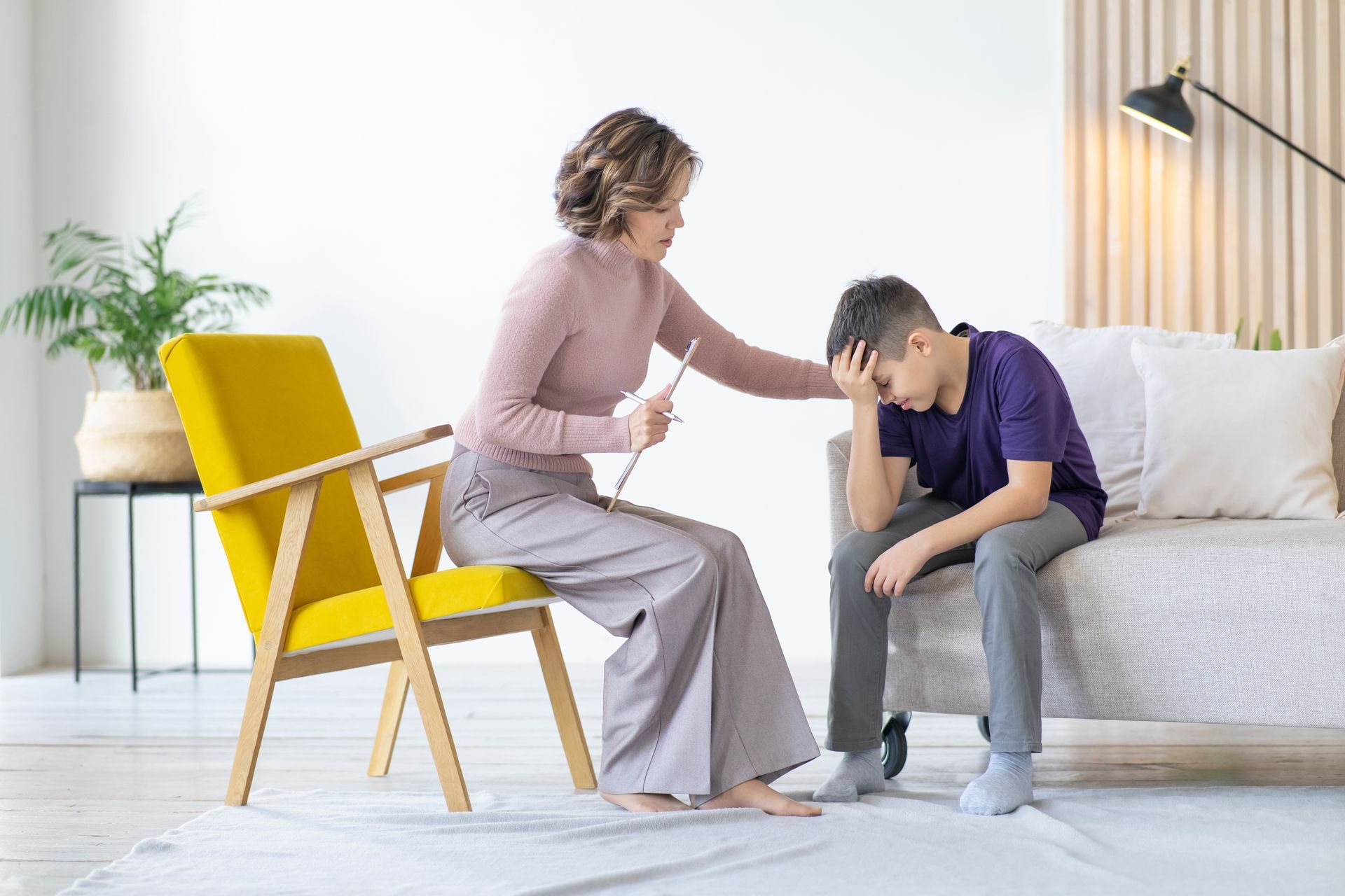 A woman is sitting in a chair talking to a boy sitting on a couch.