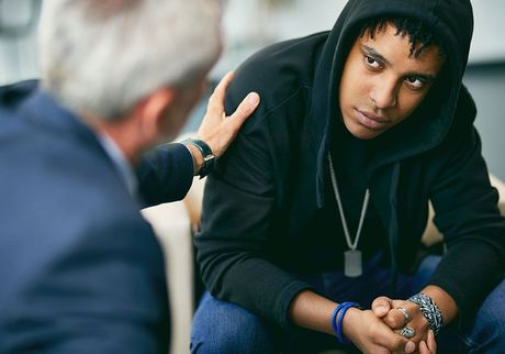 A man is comforting a young man who is sitting on a couch.