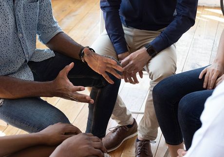 A group of people are sitting in a circle on the floor talking to each other.