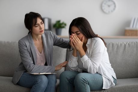 A woman is comforting another woman who is crying while sitting on a couch.