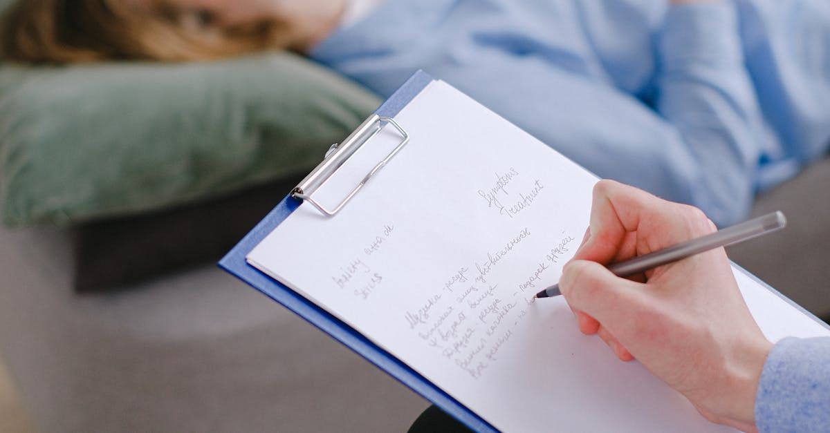 A woman is laying on a couch while a person writes on a clipboard.