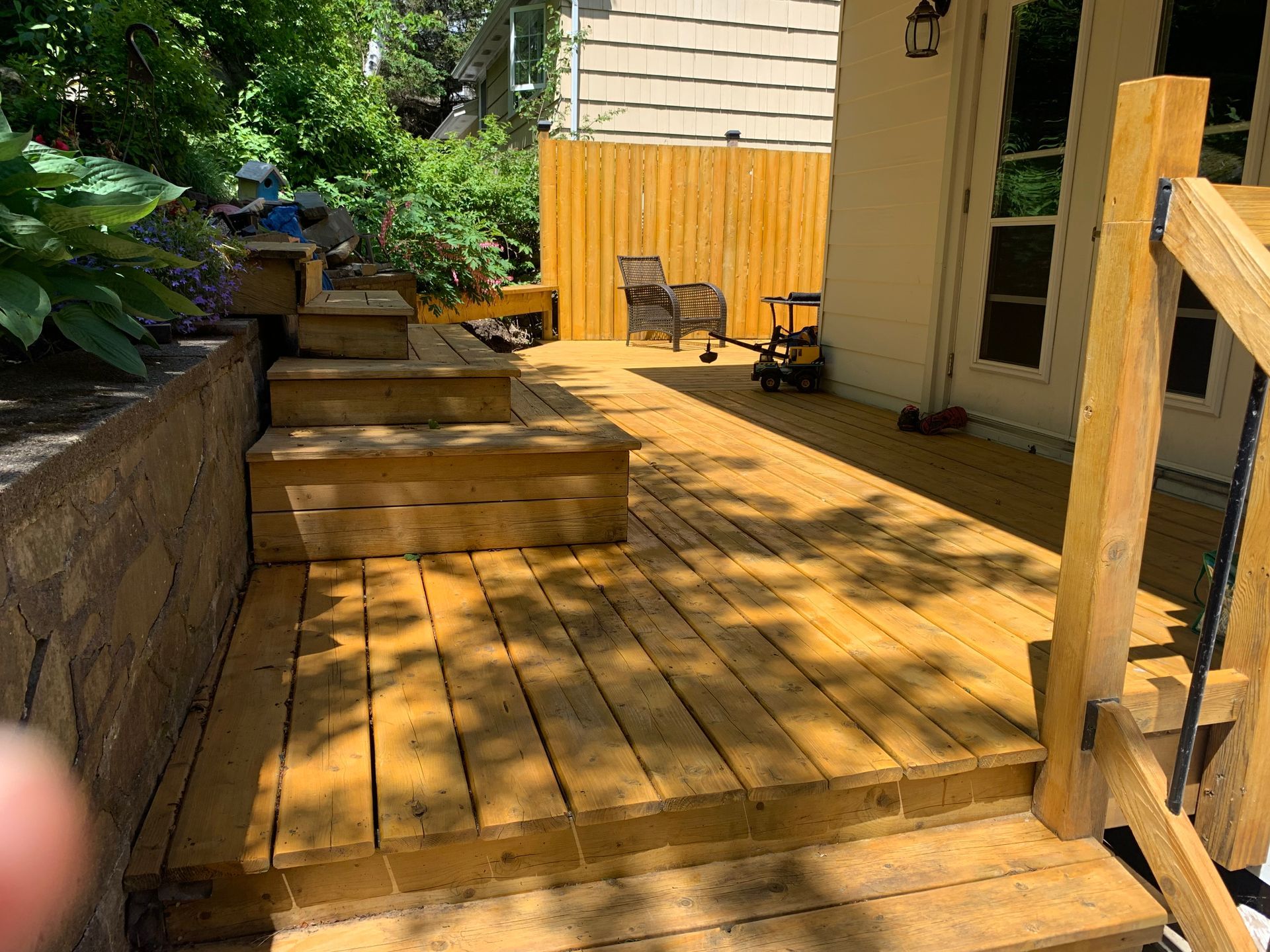 Wooden deck with steps, a fence, and a house in the background. Toys are on the deck.