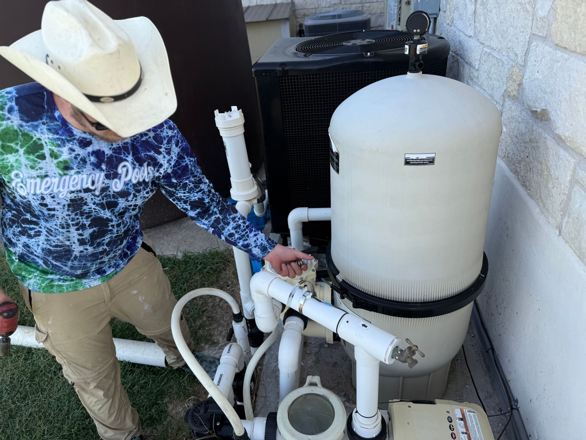 Person in cowboy hat works on pool equipment outdoors.