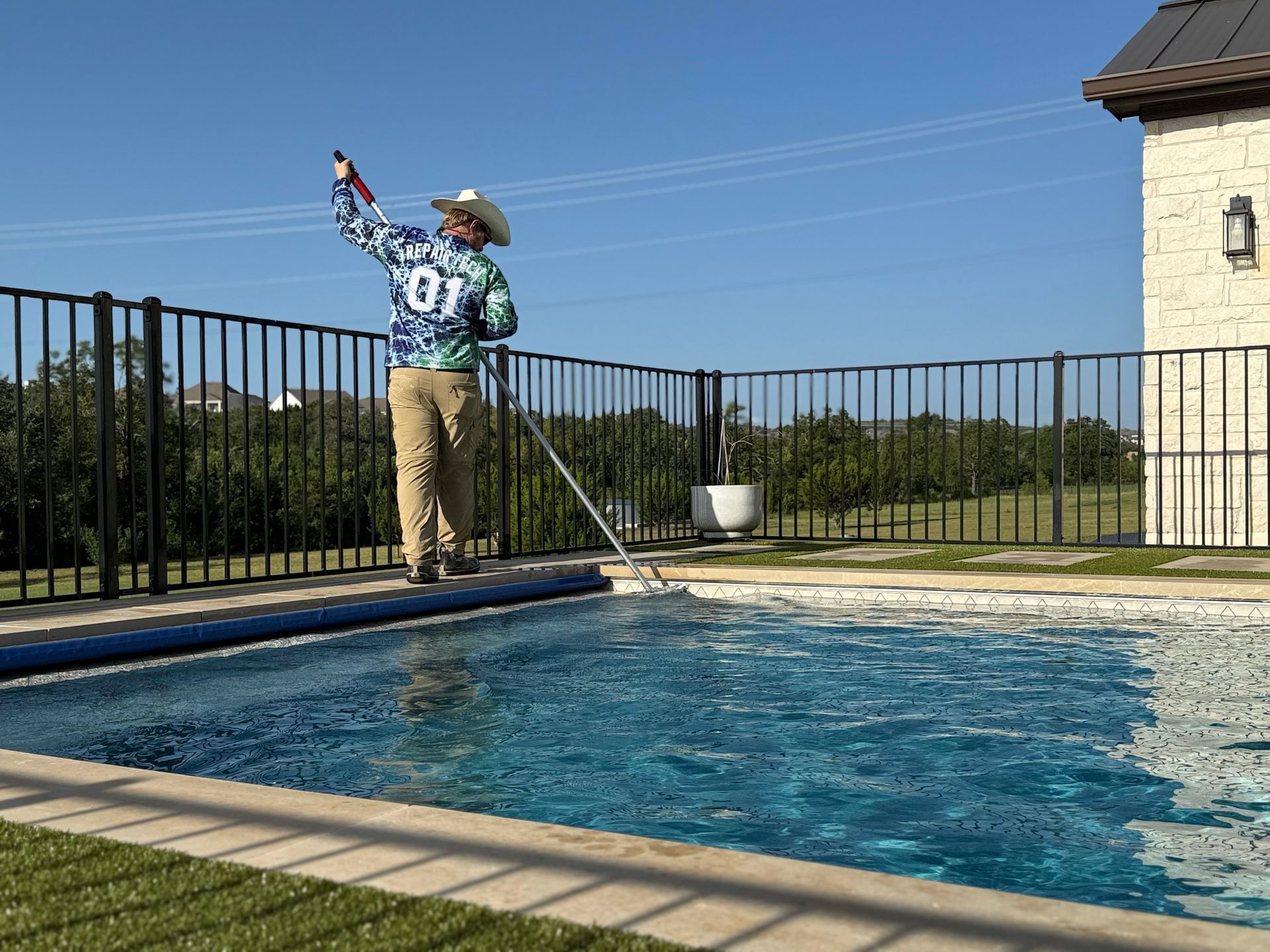 Man in cowboy hat cleaning a pool with a net, outdoors in sunlight.